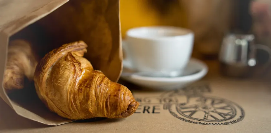 Brownbag mit Croissants und Kaffee auf einem Tisch